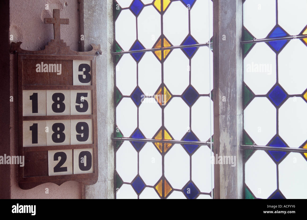 Board zeigt ausgewählte Hymne Zahlen an Rosa Wand hängen neben gefrostet Bleiglasfenster mit farbigen rautenförmige Einsätze Stockfoto