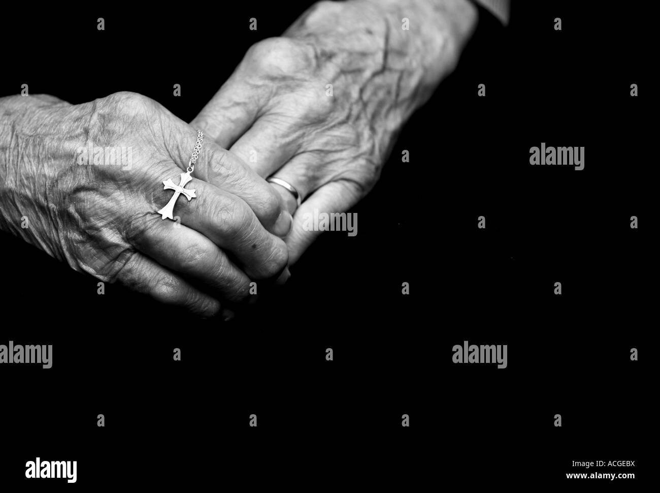 Hundert Jahre alte Damen Hände halten ein silbernes Kreuz. Schwarz / weiß Stockfoto
