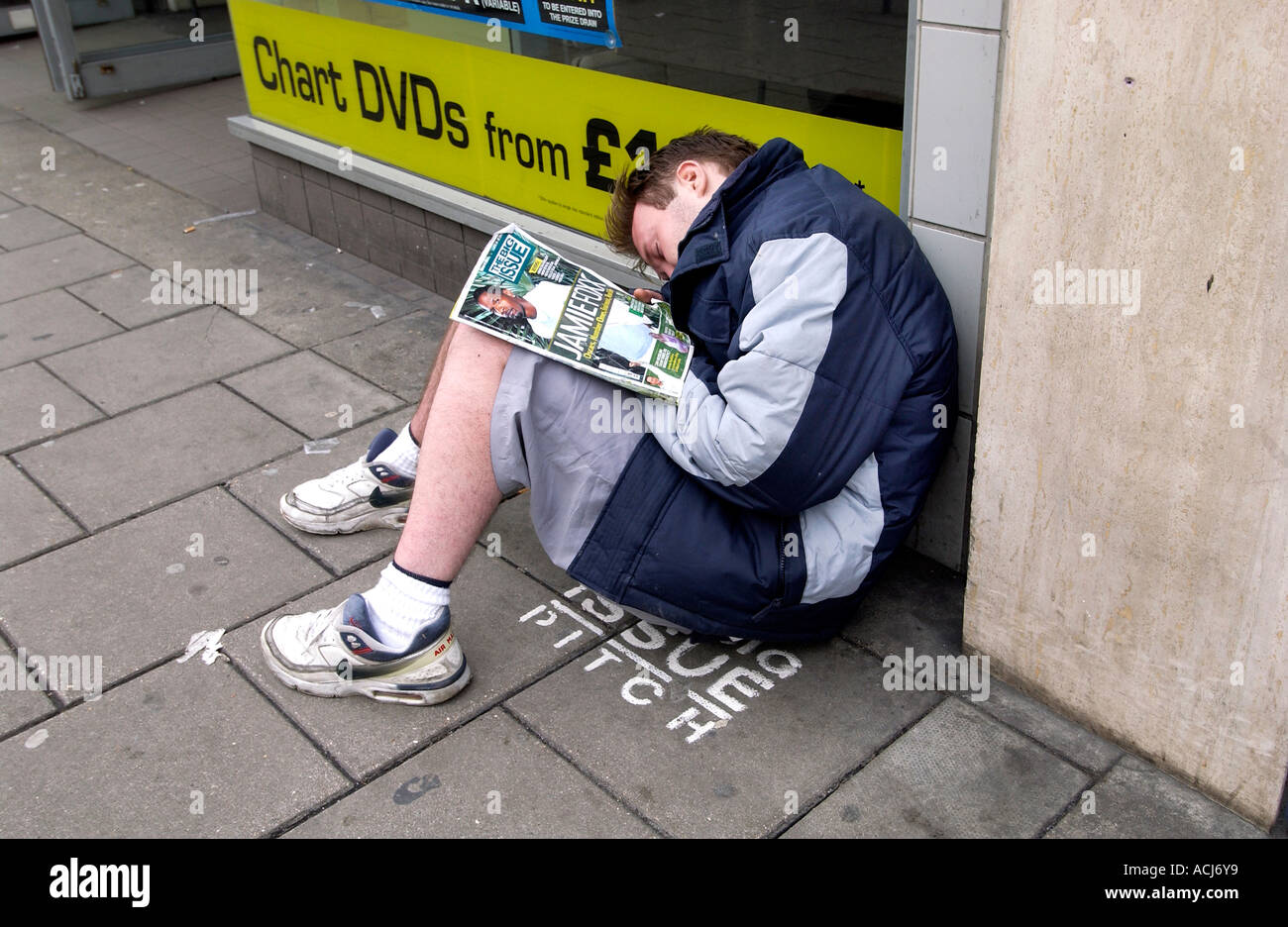 Ein Big Issue Verkäufer schlafend auf seinem Stellplatz außerhalb einen Plattenladen HMV in Western Road Brighton Stockfoto
