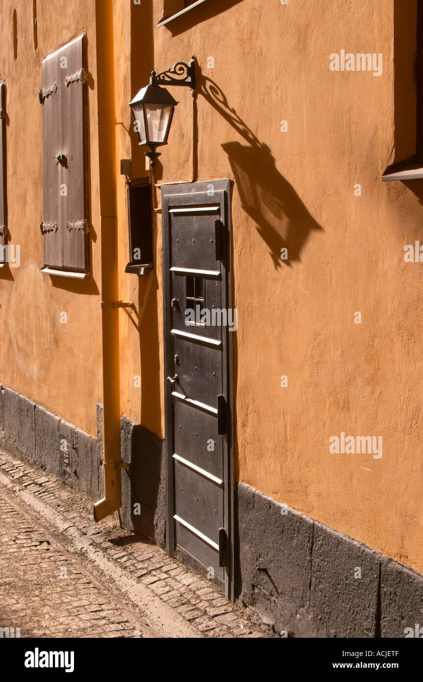 Eine gepflasterte Straße in Gamla Stan, die Altstadt von Stockholm. eine eiserne Kellertür und eine alte Lampe wirft einen langen Schatten auf die Terrakotta Wand-Stockholm, Schweden, Sverige, Europa Stockfoto