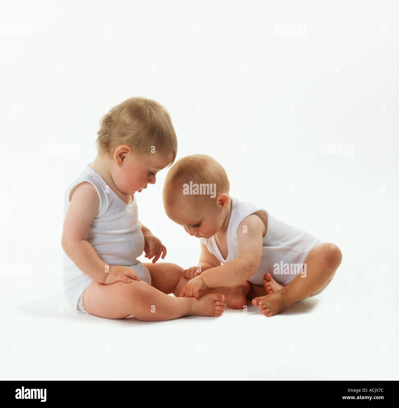 Babys Jungen und Mädchen im Alter von ca. 9 Monaten in weißen Westen sitzen auf weißem Hintergrund spielen Stockfoto