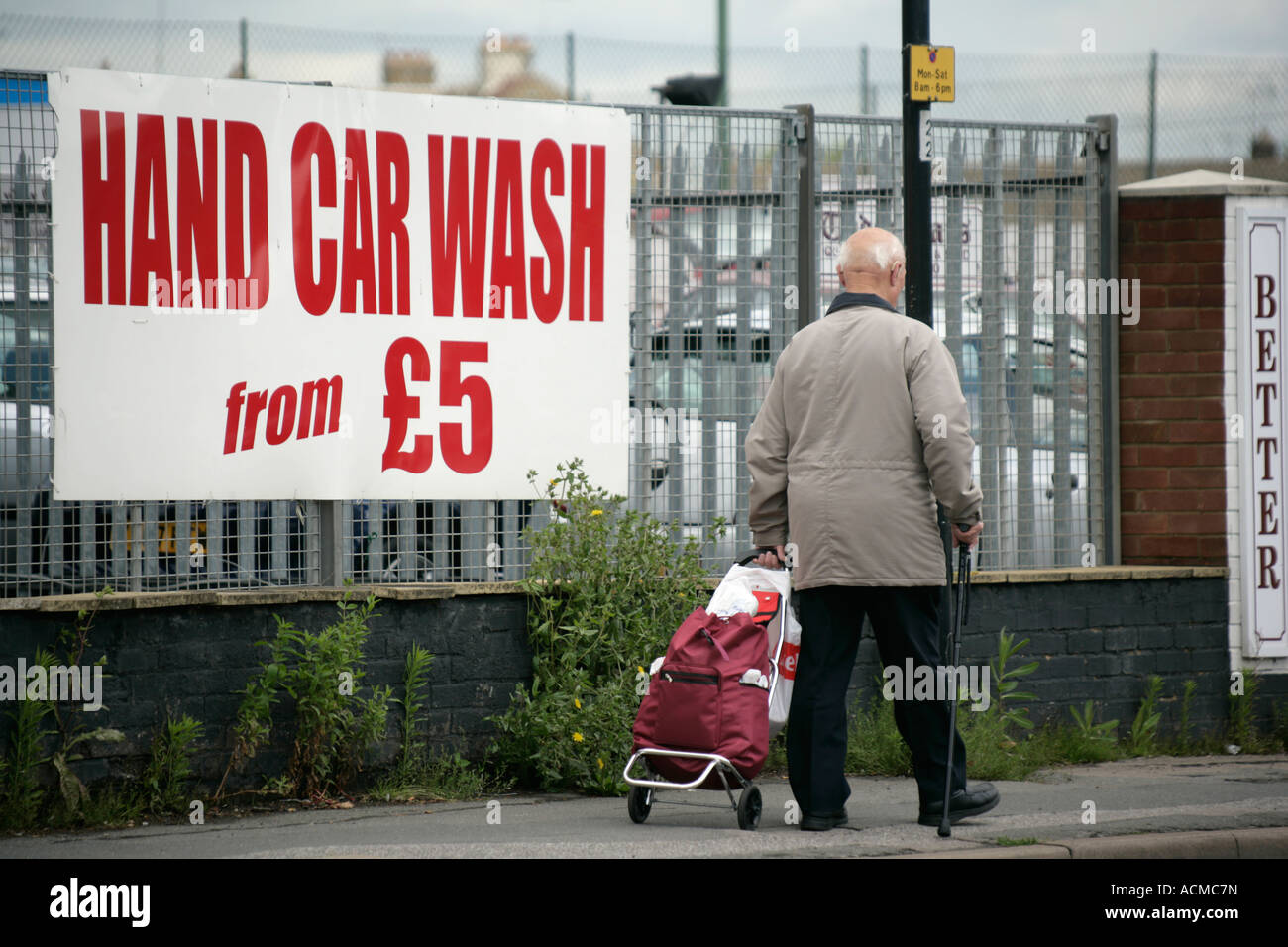 Ältere Mann schieben Einkaufswagen vorbei an einer Auto-Waschanlagen-Werbeschild, England UK Stockfoto