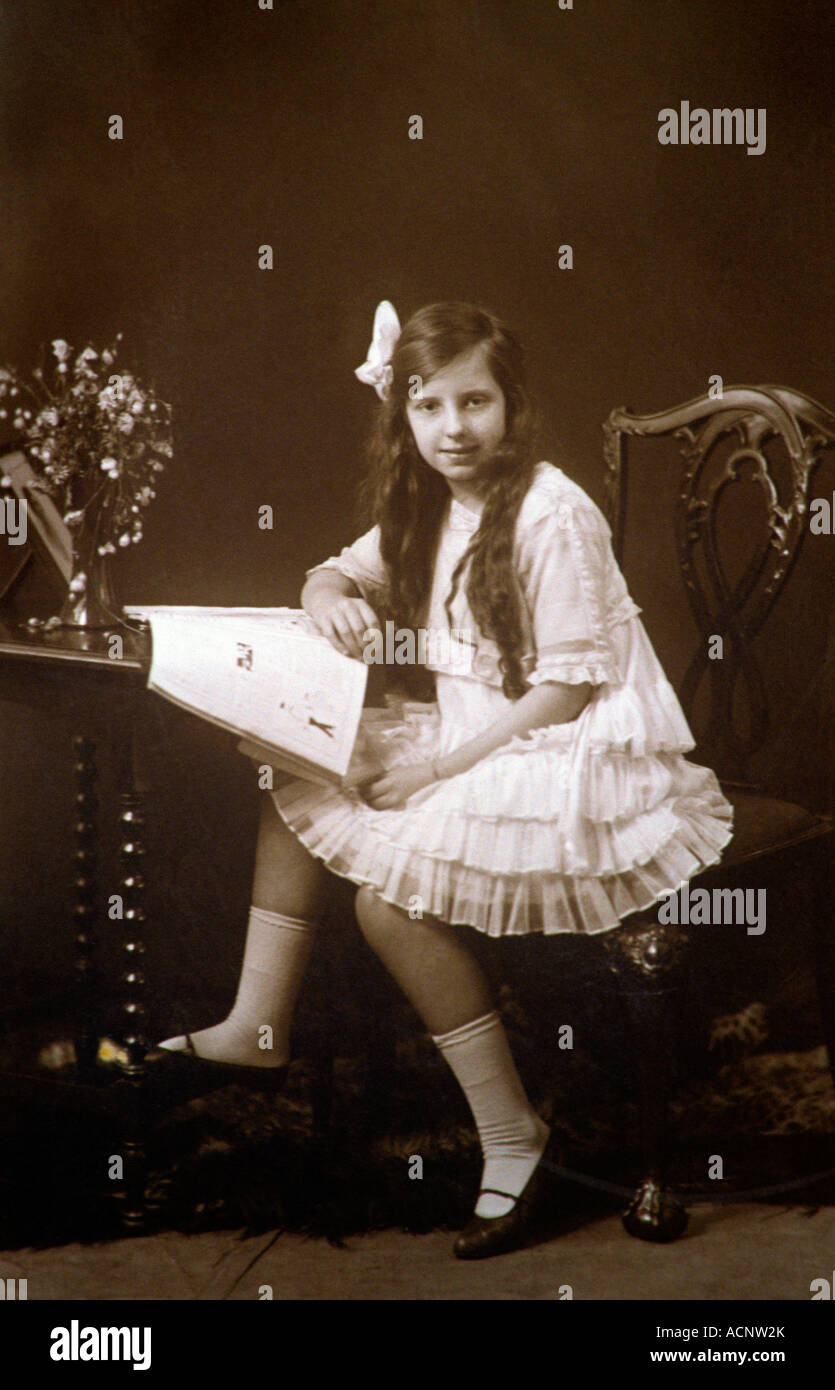 Studioportrait von edwardian Mädchen im weißen Kleid saß am Tisch Stockfoto