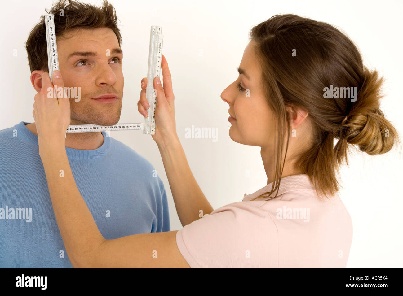 Frau, messen das Gesicht des Mannes mit Lineal, lächelnd, Nahaufnahme Stockfoto