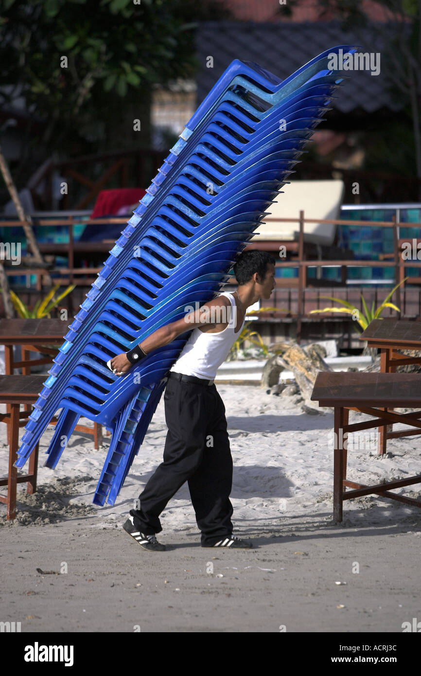 Mann trägt Haufen Plastikstühle beim Einrichten von Strand Esstische Ko Chang Thailand Stockfoto