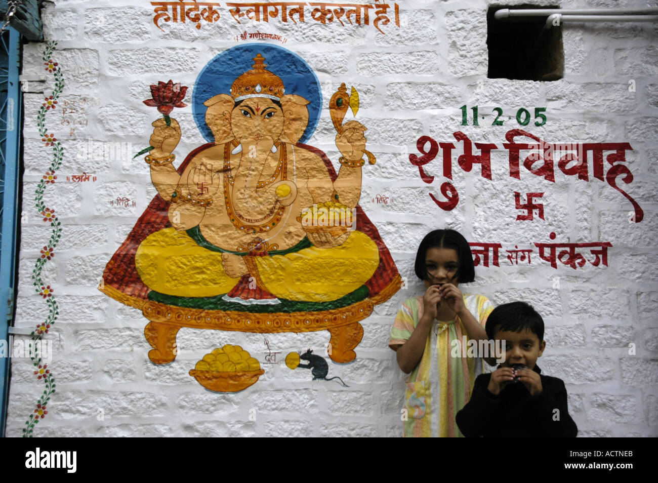 Zwei Kinder stehen vor einer Hauswand gemalt mit Gott Ganesha und indischen Skript Sanskrit Jaisalmer, Rajasthan Indien Stockfoto