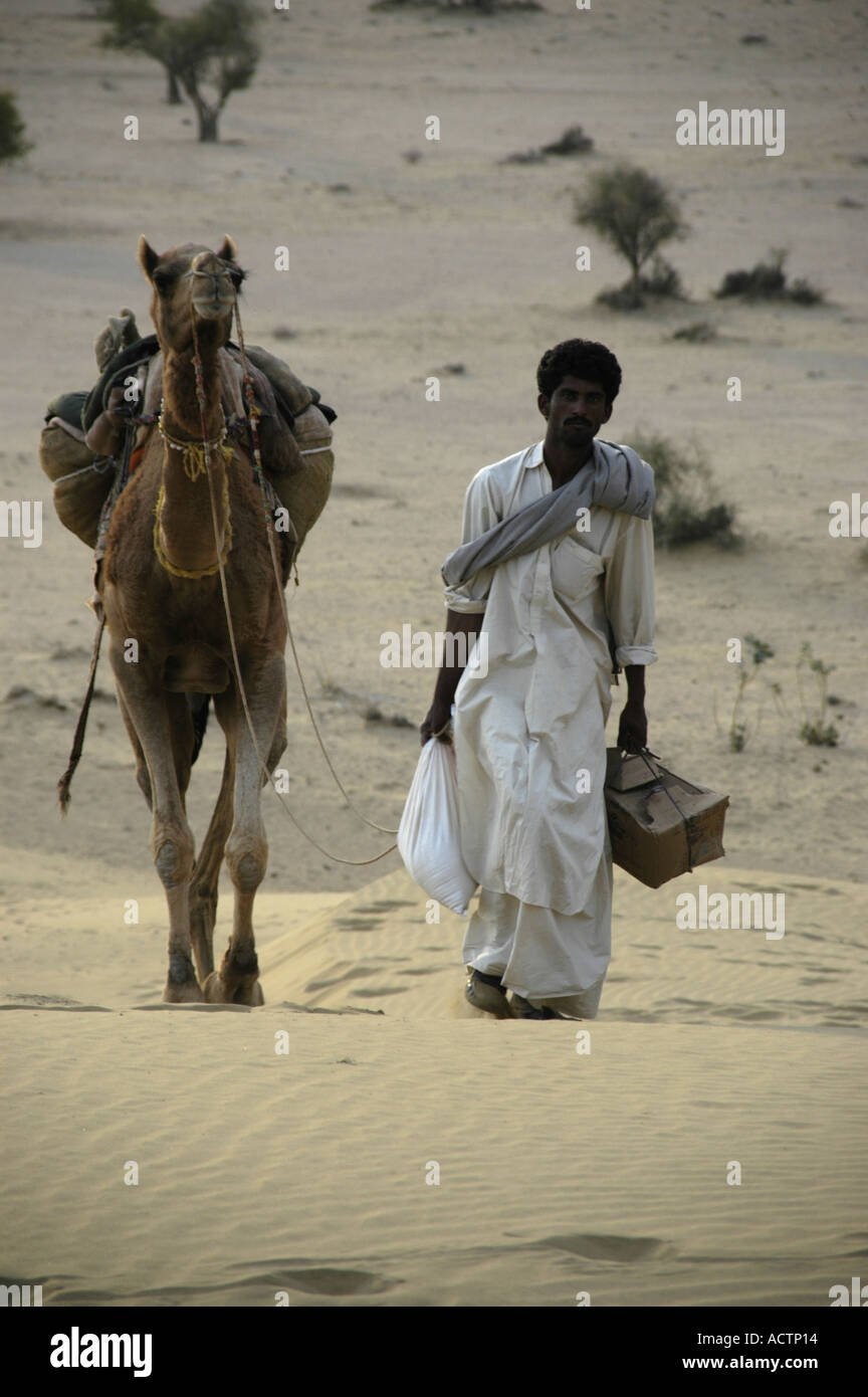 Mann in weißes Tuch gekleidet ist neben einem Kamel in den Sand in weiten, offenen Thar-Wüste in der Nähe von Jaisalmer, Rajasthan Indien Fuß Stockfoto