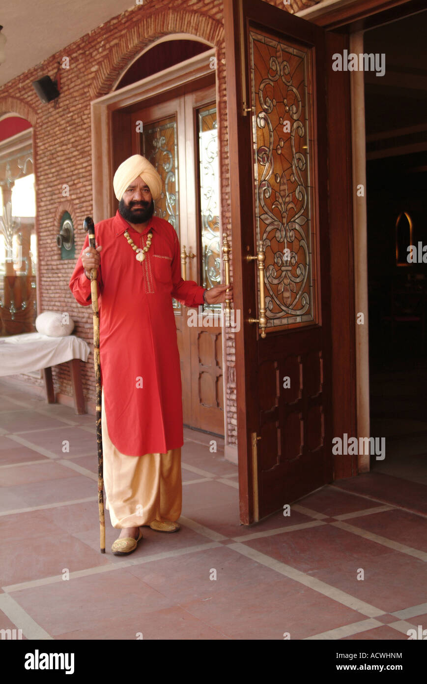 EIN SIKH KEINEN VERTRAUENSWÜRDIGEN EINDRUCK IN SEINER TRACHT PUNJABI HÄLT DIE TÜR FÜR DIE GÄSTE Stockfoto