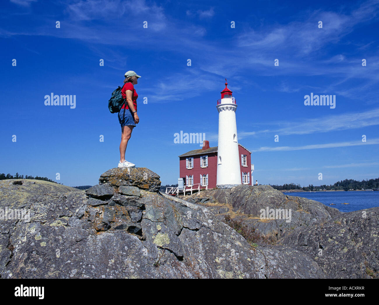Ein Wanderer entlang der felsigen Küste von BC und einen Blick auf den historischen Fisgard Leuchtturm am Fort Rodd Hill, Victoria British Columbia. Stockfoto