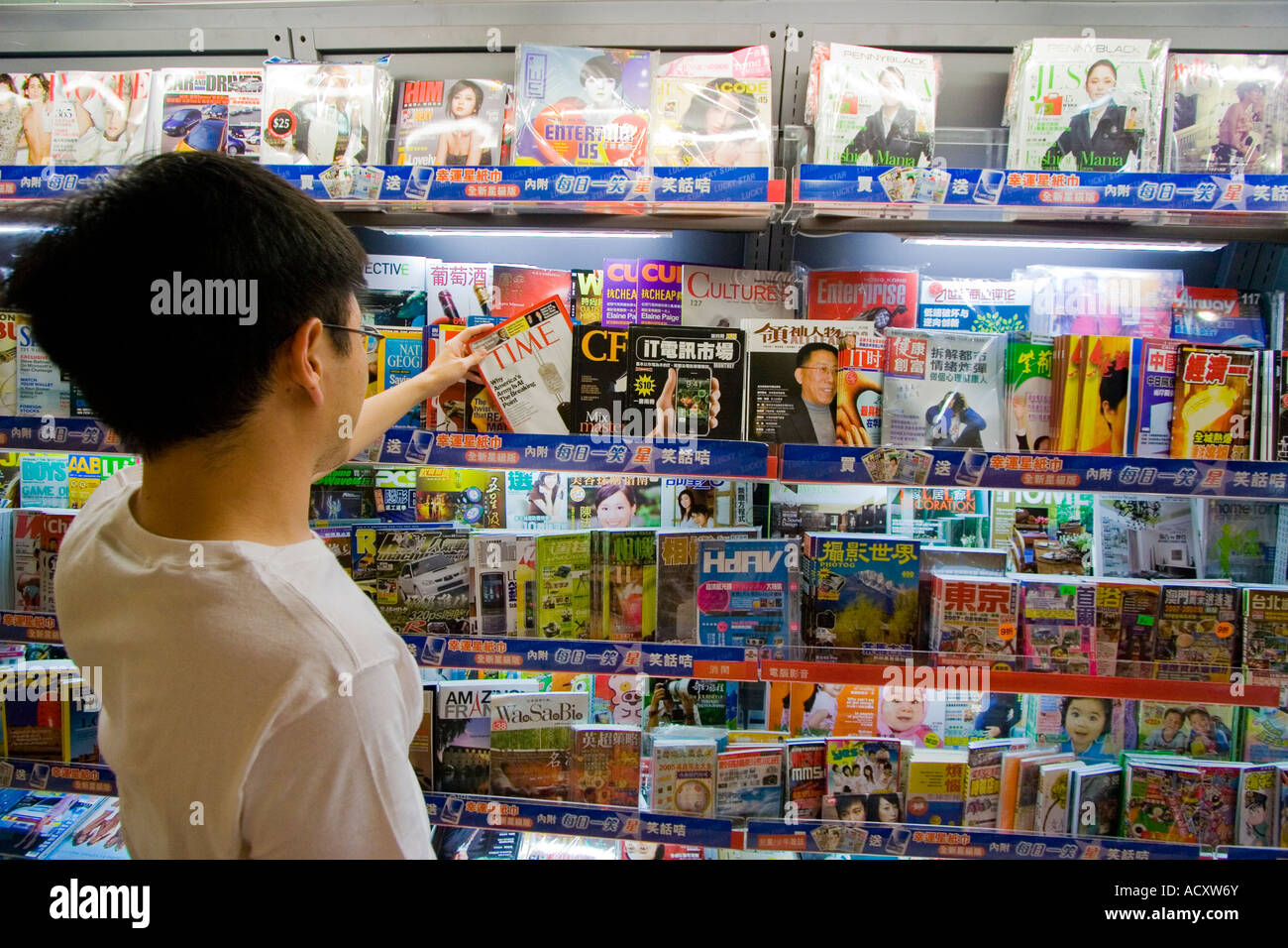 Junger Mann nimmt Zeit aus einem Zeitschriftenständer Kowloon Hong Kong Stockfoto