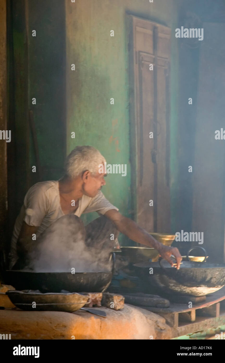 Vertikale Porträt eines alten Mannes sitzen in einem rauchigen heiße Atmosphäre Kochen mit dem Wok vor der Tür seines Hauses Stockfoto