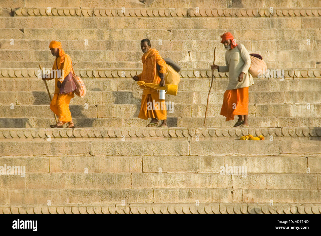 Horizontale Ansicht der drei orange Sadhus in traditionellen orange Kleidung entlang Dasashvamedha Ghat am Ufer des Flusses Ganges. Stockfoto