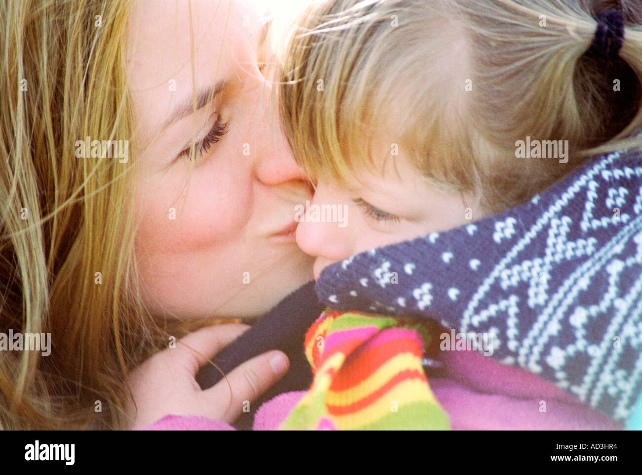 Junge Mutter ihre kleine Tochter auf die Wange küssen Stockfoto