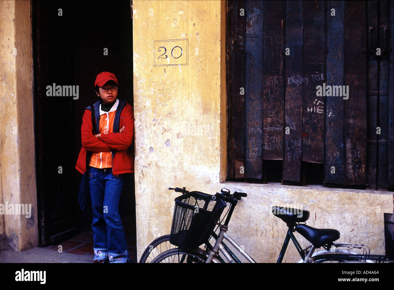 Mädchen in der Tür tragen rote gelehnt eine gelbe Wand in der Nähe von zwei Push-Bikes in Hanoi Vietnam Stockfoto