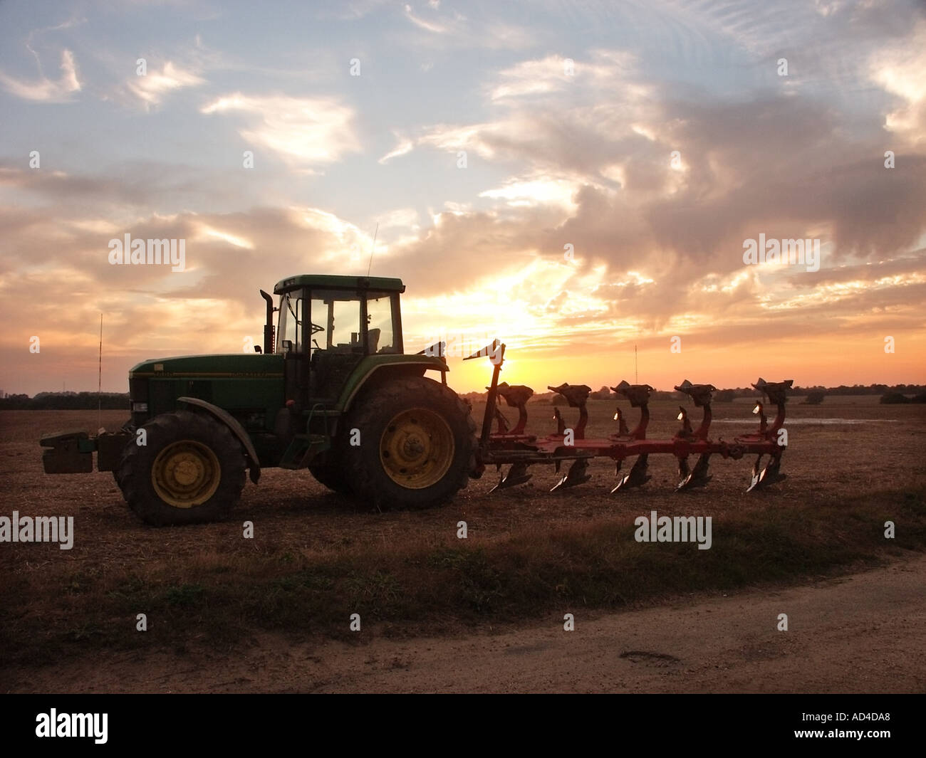 Sonnenuntergang Himmel & Silhouette des Bauern John Deere Traktor & Pflug geparkt auf Ackerland in Essex England UK Feld am Ende eines Arbeitstages Stockfoto