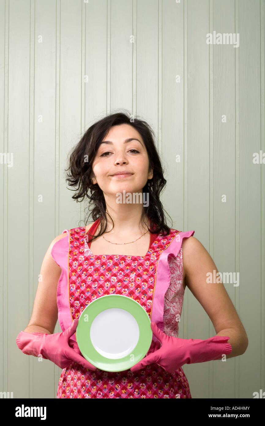 Eine Frau hält einen Teller während einer Schürze und Gummihandschuhe tragen Stockfoto