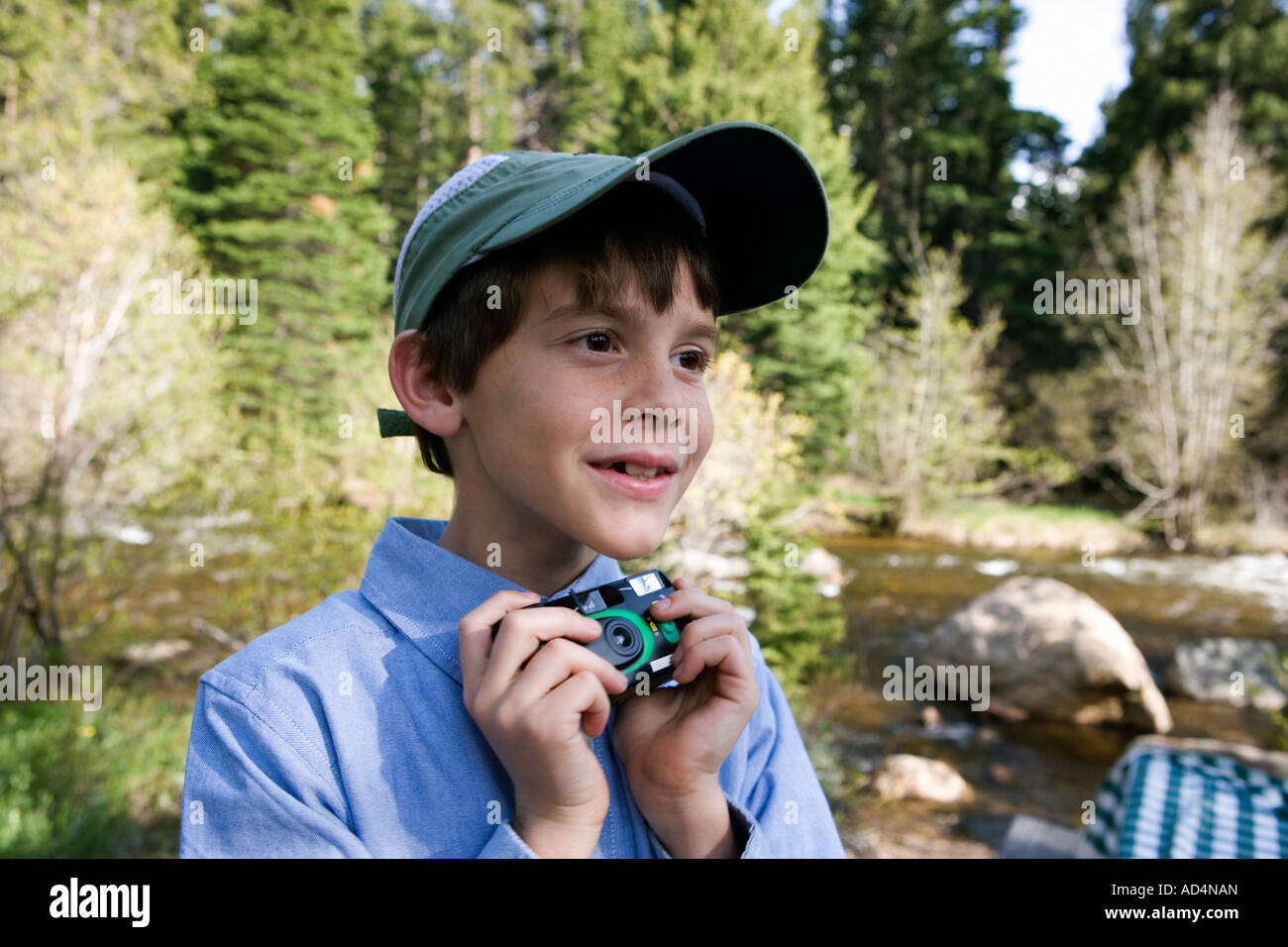 Ein kleiner Junge hält eine Einweg-Kamera an einem Fluss Stockfoto
