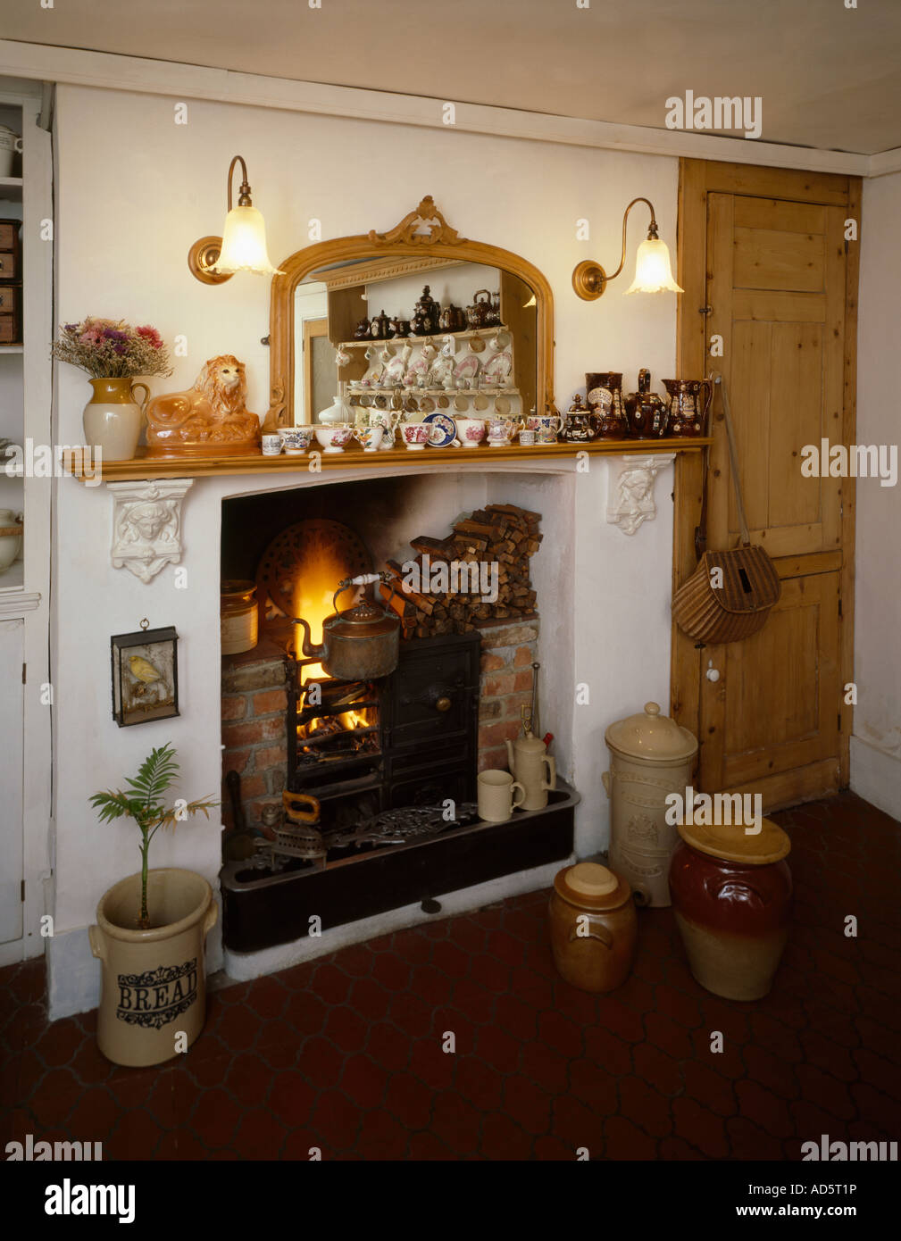 Wandleuchten mit Glasschirmen auf beiden Seiten des Spiegels über Kamin mit Wasserkocher auf Gusseisen Stockfoto