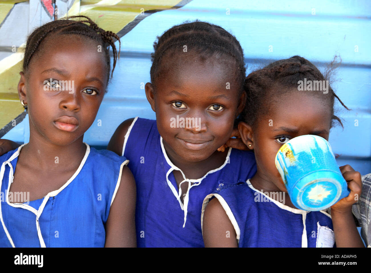 Horizontale helle Farbe Porträt oder drei Kinder in Sierra Leone, sitzen mit blauen Holzlatte Mauer gemalt mit Sardine Anzeige Stockfoto
