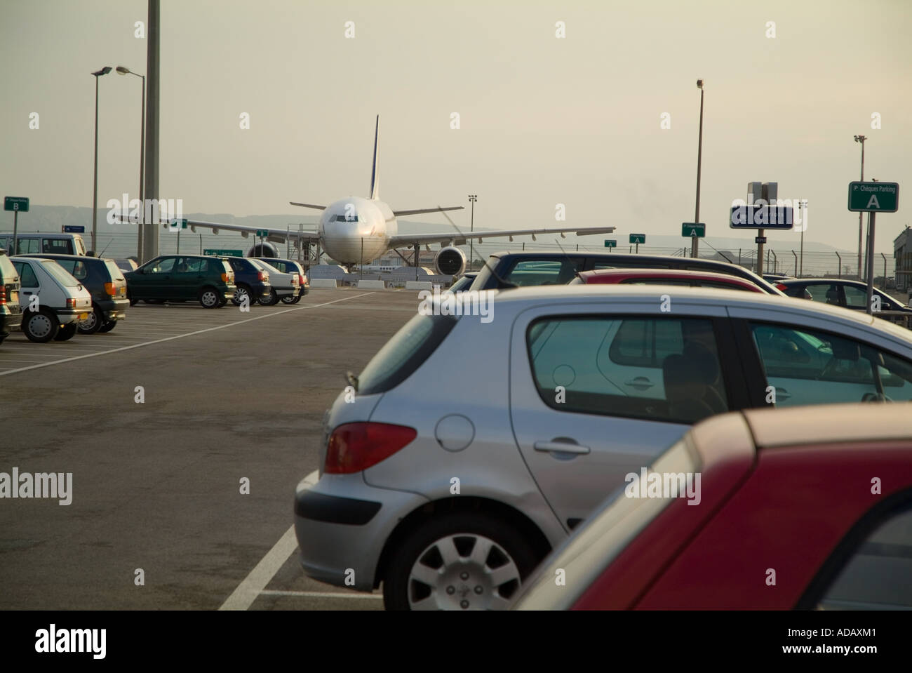 Geparkte Autos und ein Flugzeug bei Sonnenuntergang an der Flughafen Marseille Provence, Marignane, Marseille, Frankreich. Stockfoto