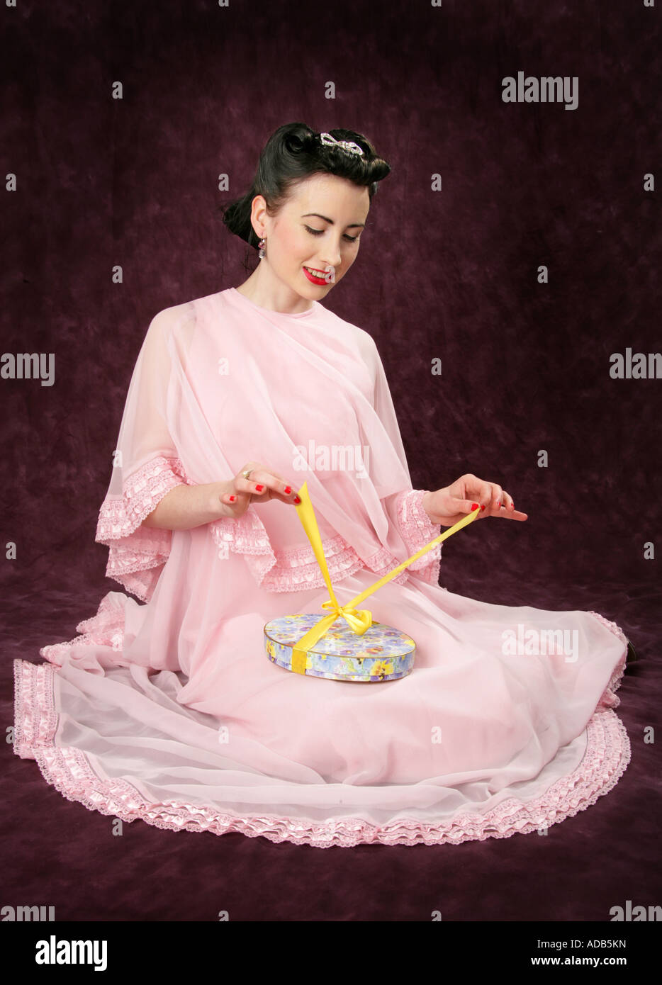 Pin Up Girl in einem rosa Kleid Öffnung eine Schachtel mit Süßigkeiten mit einer gelben Schleife gebunden Stockfoto