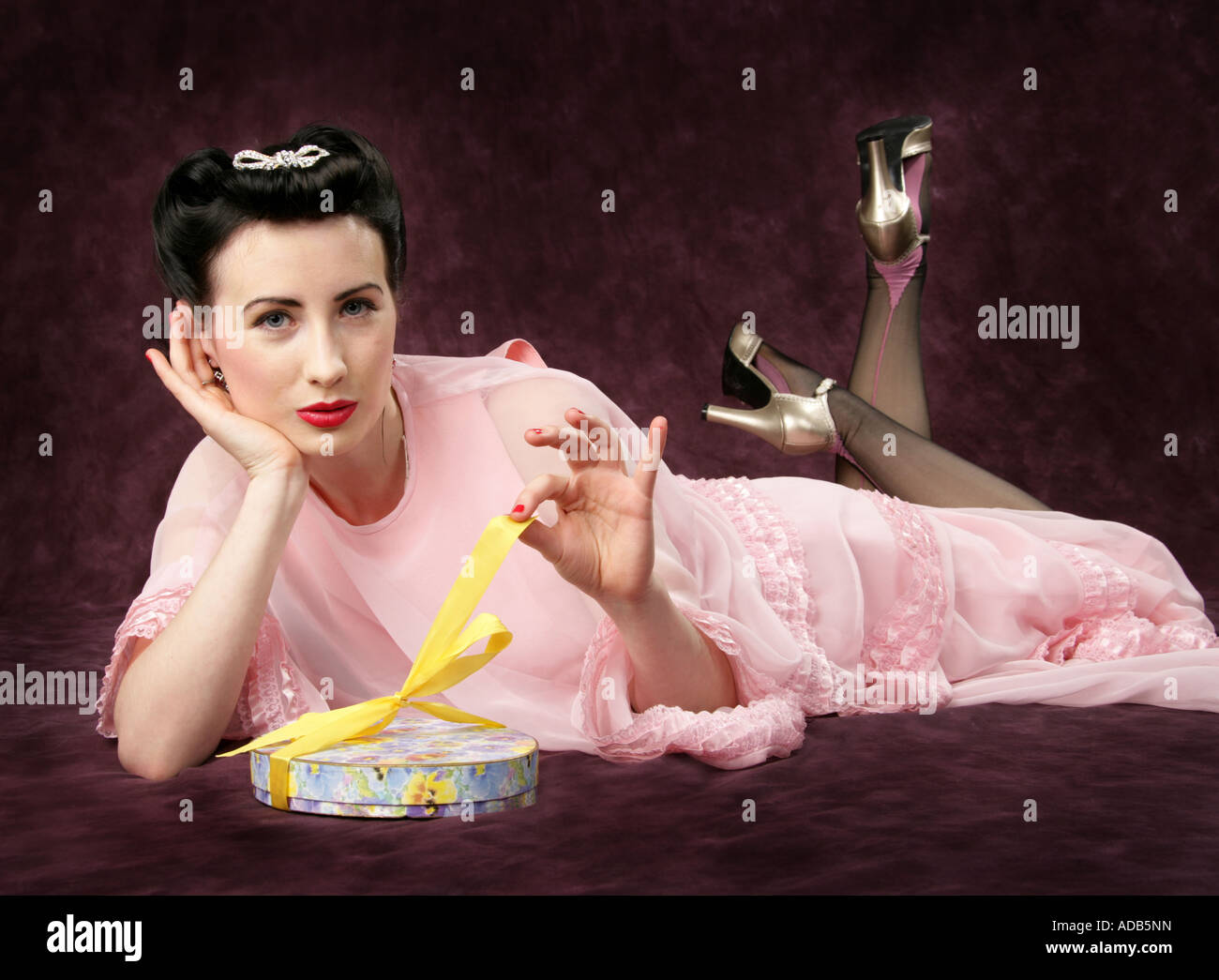 Pin Up Girl in einem rosa Kleid Öffnung eine Schachtel mit Süßigkeiten mit einer gelben Schleife gebunden Stockfoto