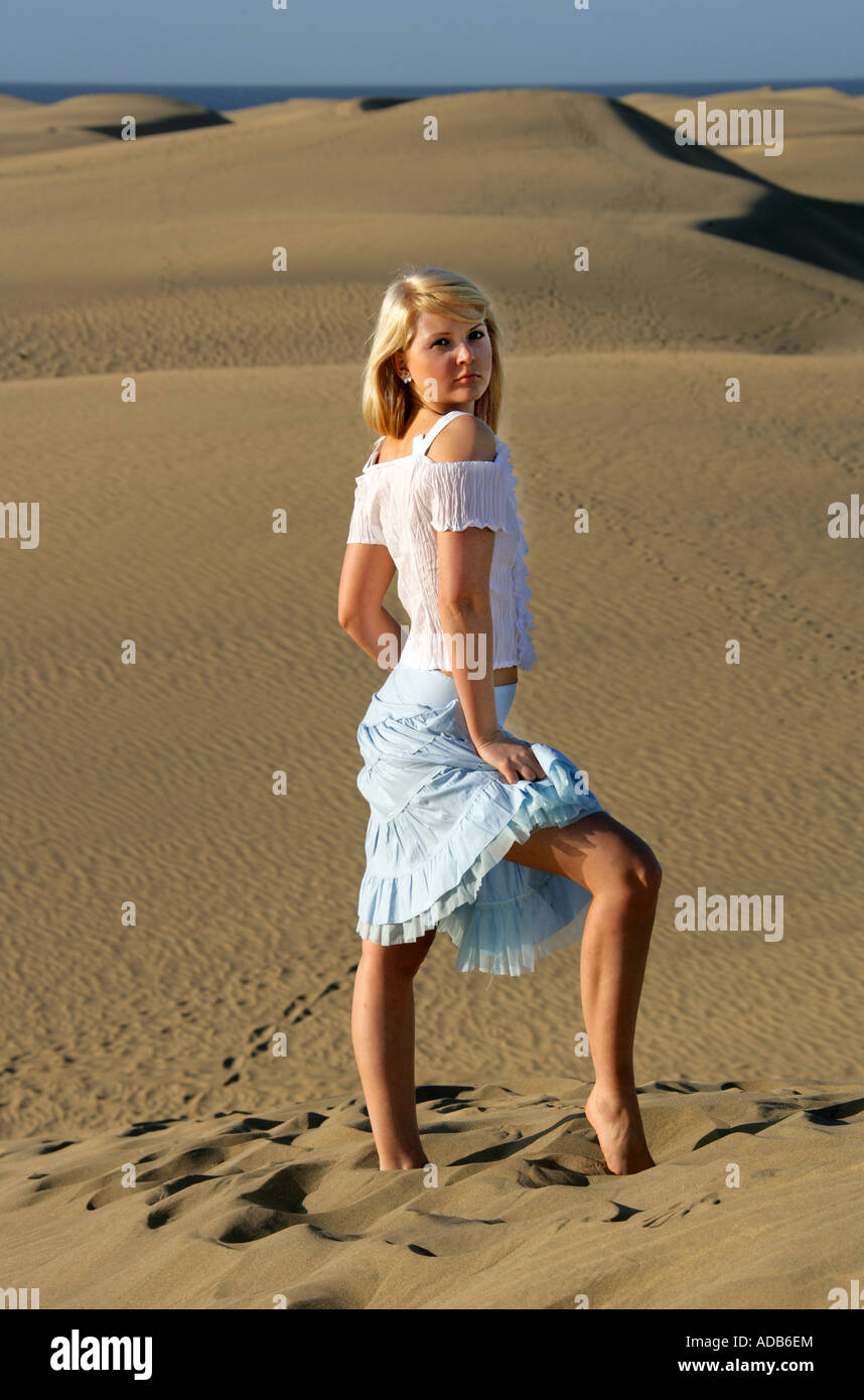 Blondes Mädchen mit einem weißen Top und blauen Rock auf Sanddünen stehen Stockfoto