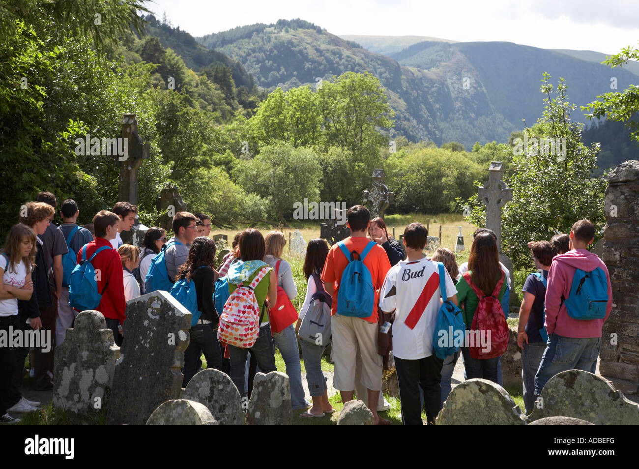 Gruppe von Jugendlichen und Jugendlichen rund um Kloster Glendalough Website und Friedhof von Reiseleiter angezeigt wird Stockfoto