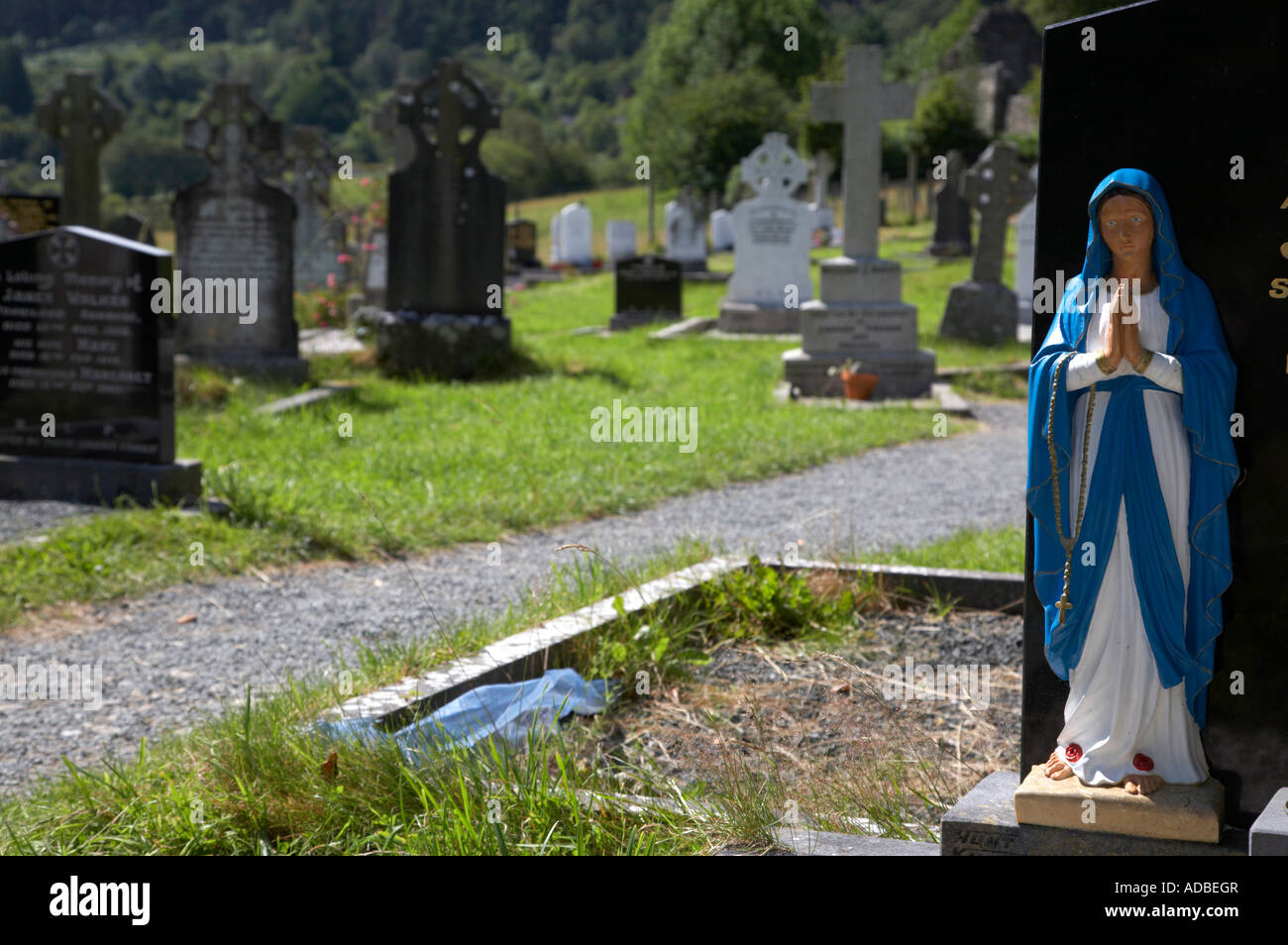 blaue und weiße Statue unserer lieben Frau der Jungfrau Maria beten sitzen oben auf Grab auf dem Friedhof Glendalough klösterlichen Website Stockfoto