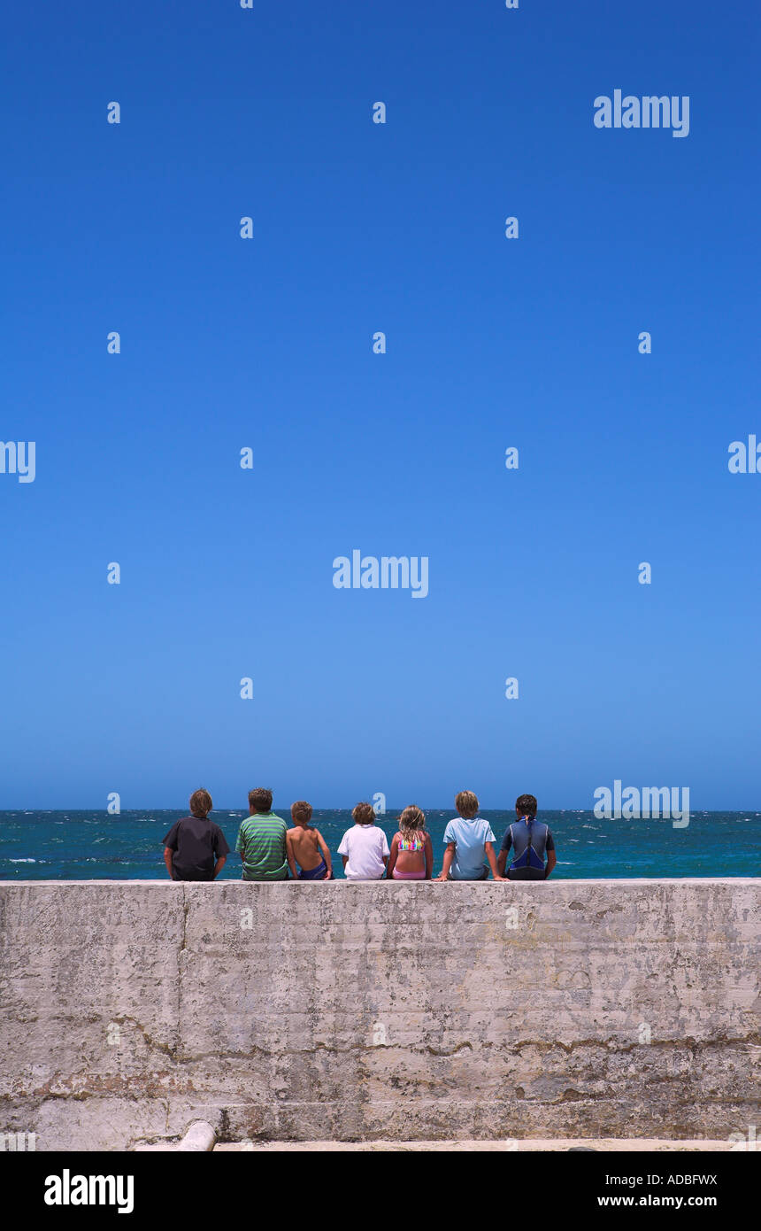 Sieben Freunde sitzen zusammen auf der Hafenmauer Wellenbrecher Stockfoto