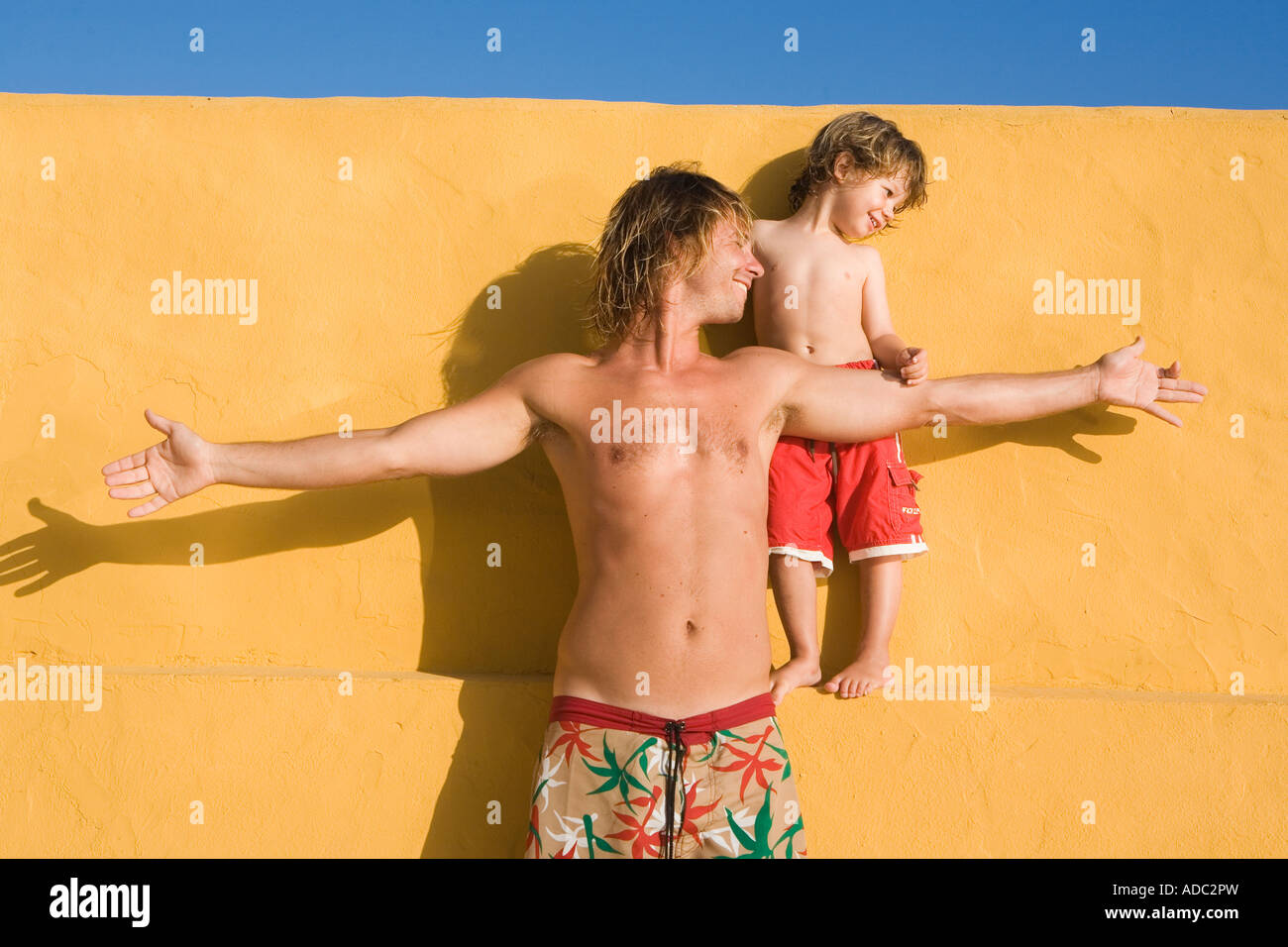 Vater und Sohn spielen zusammen auf eine gelbe Wand Agianst blauen Hintergrund Stockfoto