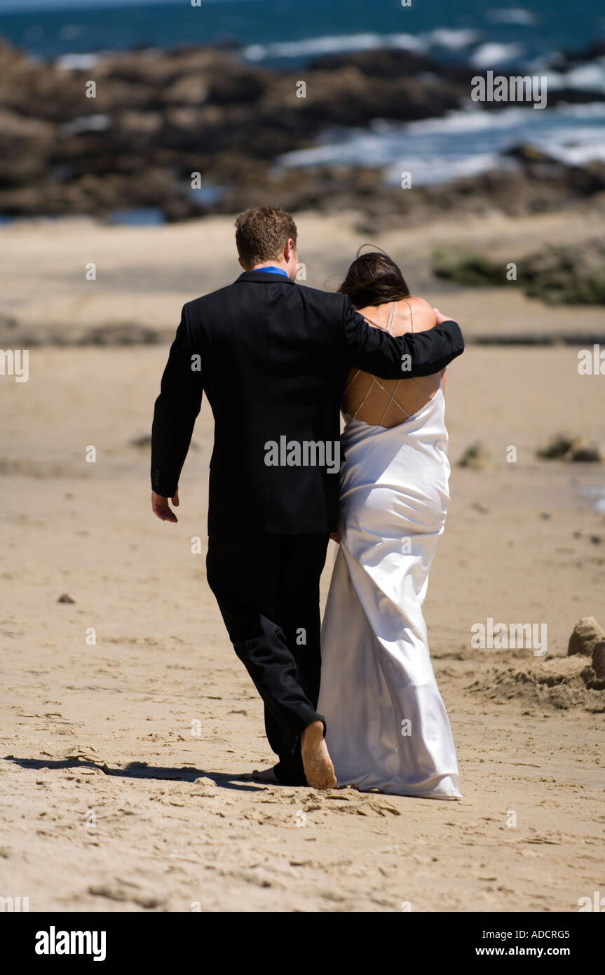 Frisch verheiratete Paar am Strand entlang in Richtung des Ozeans, die Hand in Hand Stockfoto