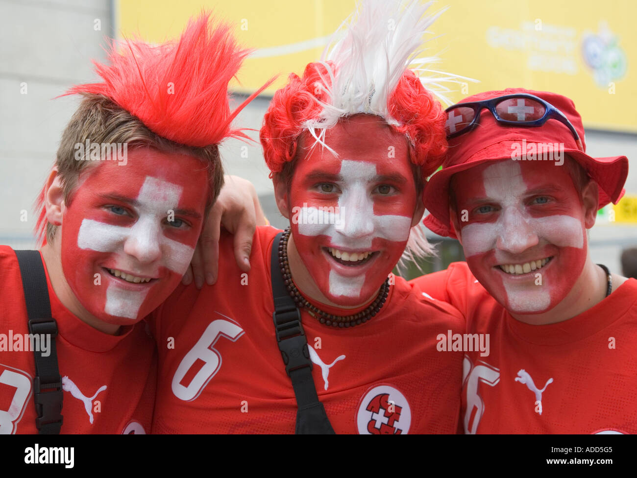 Drei Schweizer Fußball-Fans mit Make-up in ihren Landesfarben, lächelnd in gute Laune Stockfoto