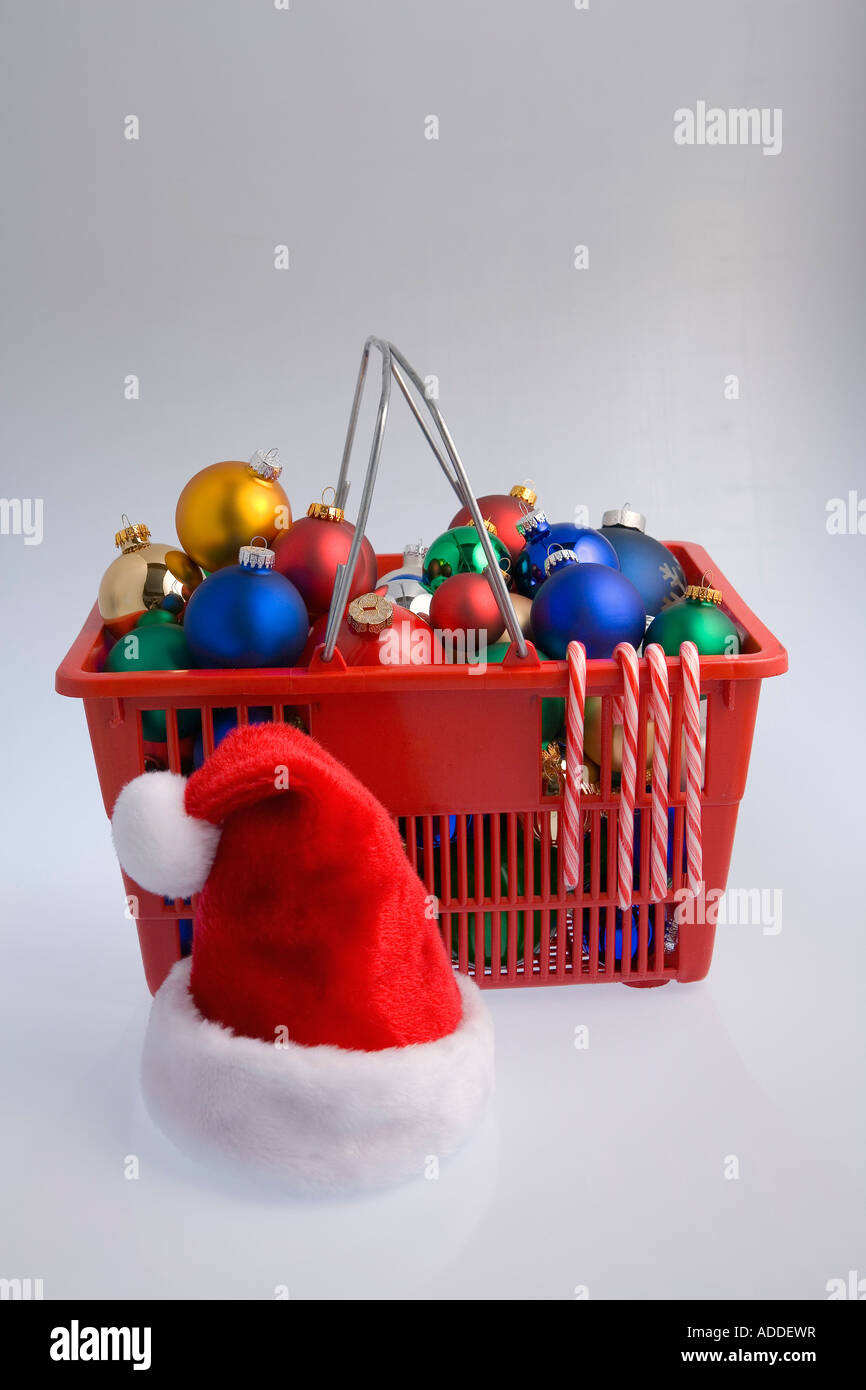 Warenkorb gefüllt mit bunten Weihnachtsbaum Birne Ornamente Zuckerstangen und Weihnachtsmütze auf weißem Hintergrund Studioportrait Stockfoto