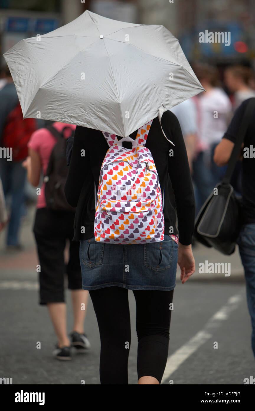 Frau im kurzen Jeansrock tragen einen hellen Rucksack trägt einen Regenschirm über die Straße am Fußgängerüberweg auf oconnell Stockfoto