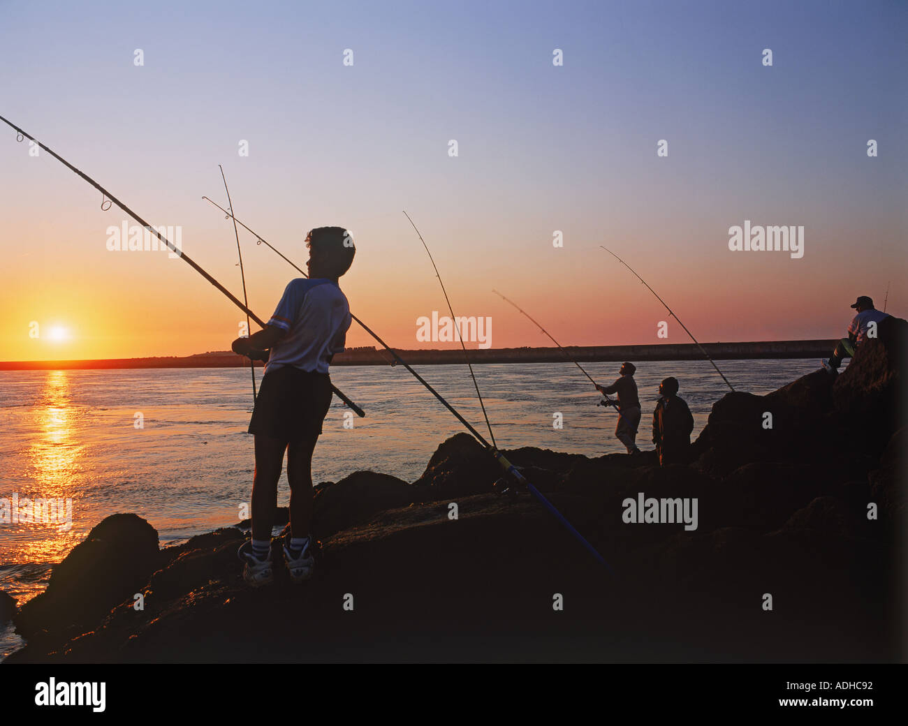 Männer, die Fischerei vor felsigen Steg am Sonnenuntergang Portugal Stockfoto