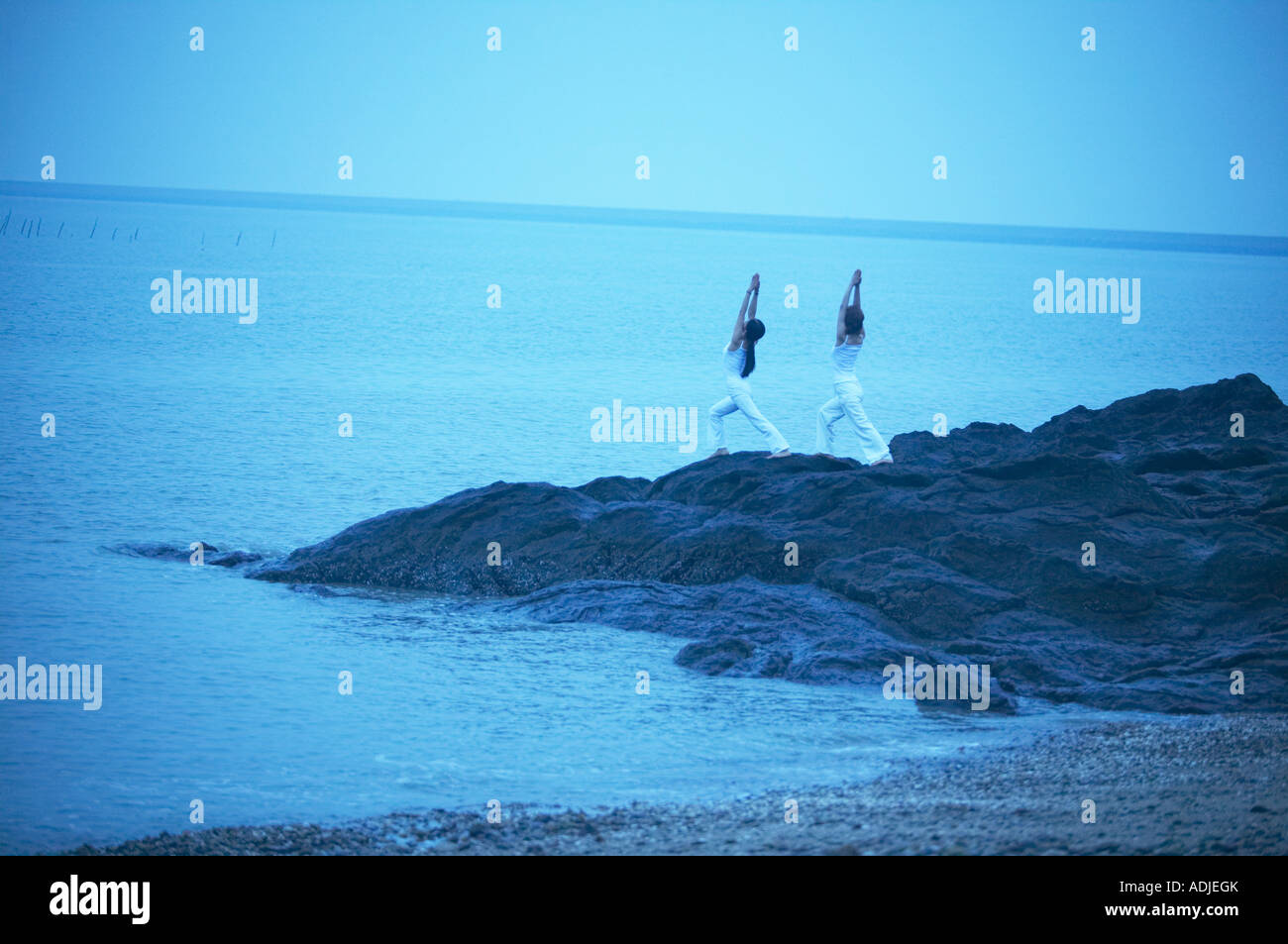 eine Frau tut Yoga auf den Felsen in einem Meer Stockfoto