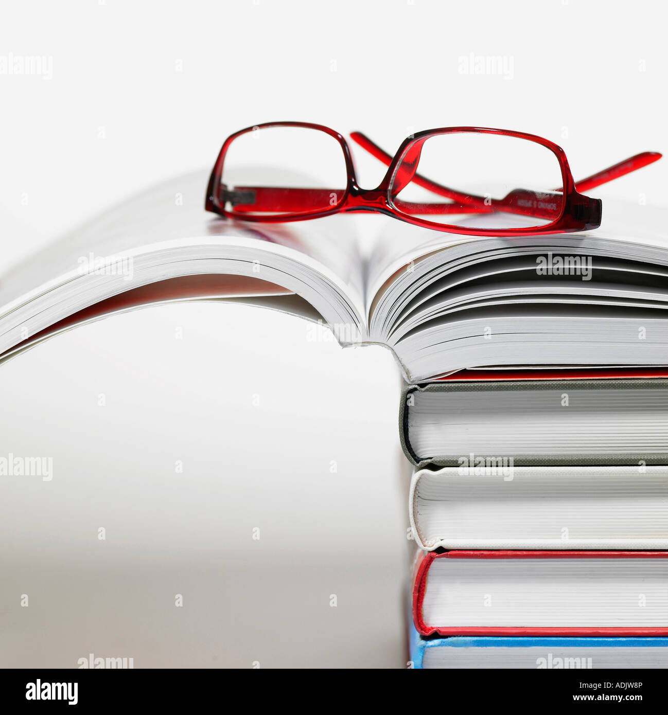 Gläser auf einem geöffneten Buch über die gestapelten Bücher Stockfoto