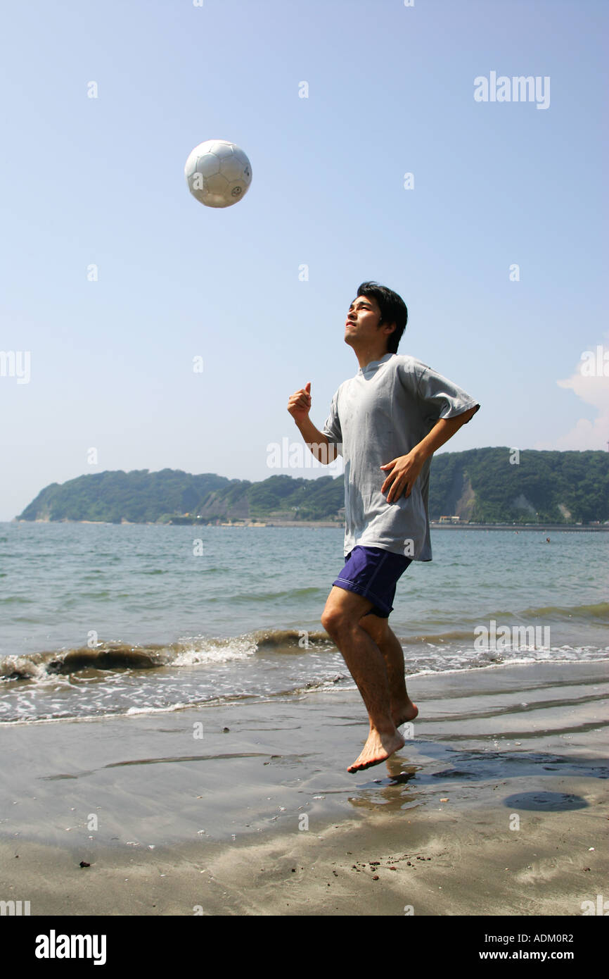 Junger Mann spielen Fußball am Strand Stockfoto