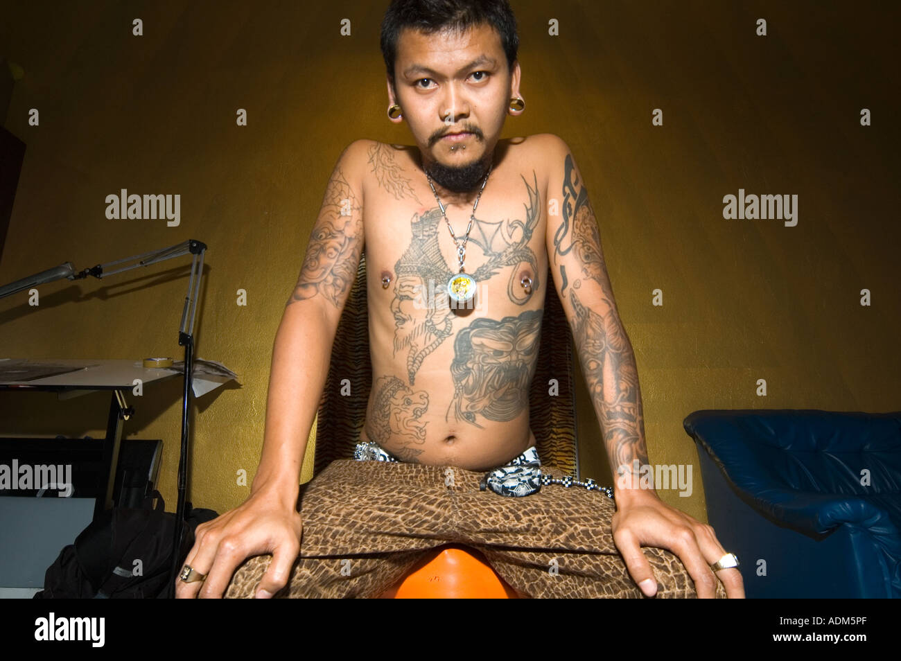 Thai Tätowierer sitzt auf seinem Schemel zwischen tätowieren Sitzungen in seiner Stube in Chiang Mai, Nordthailand. Stockfoto