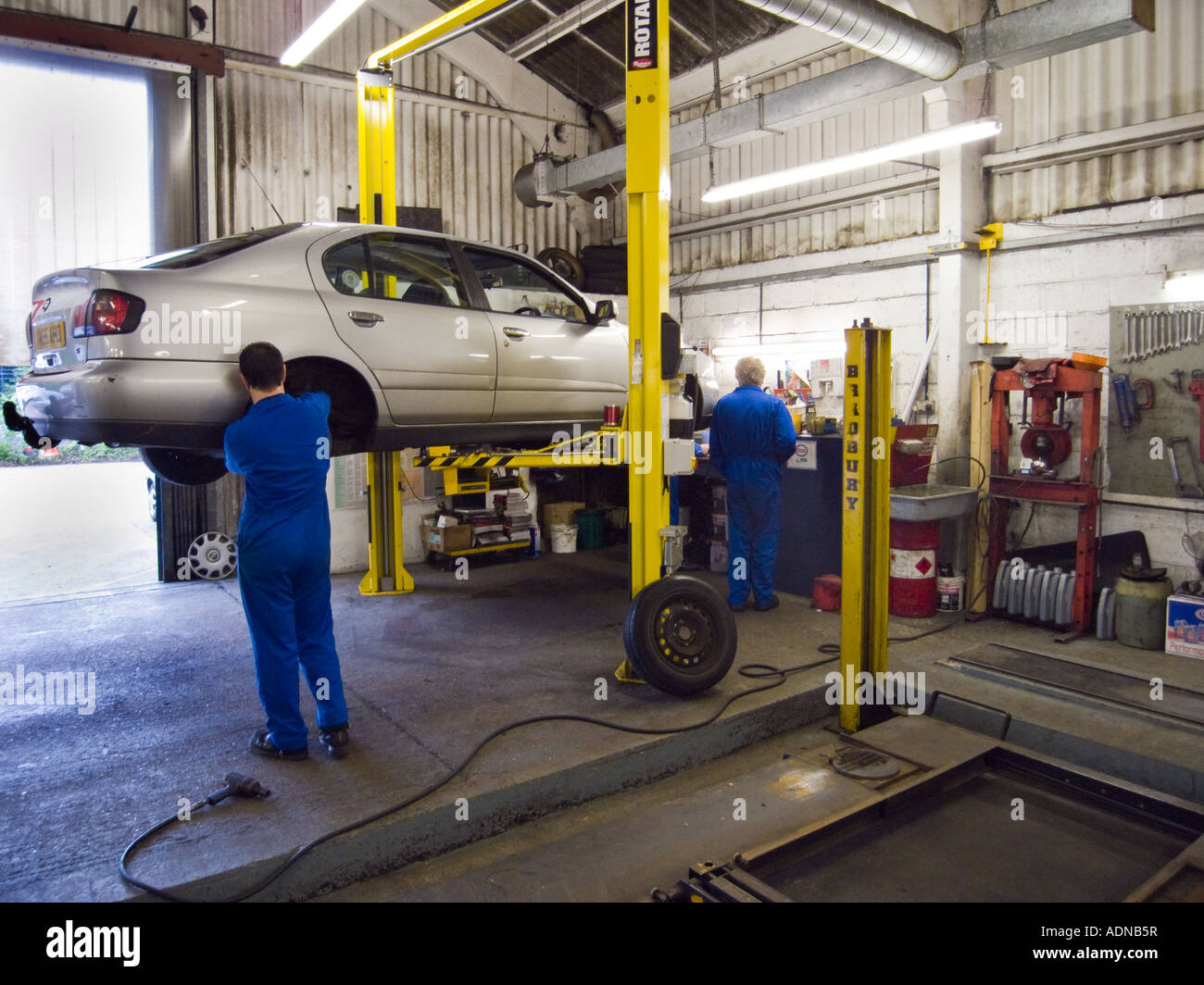 2 Kfz-Mechaniker in einer Autowerkstatt mit hydraulischen Auto arbeiten heben Stockfoto