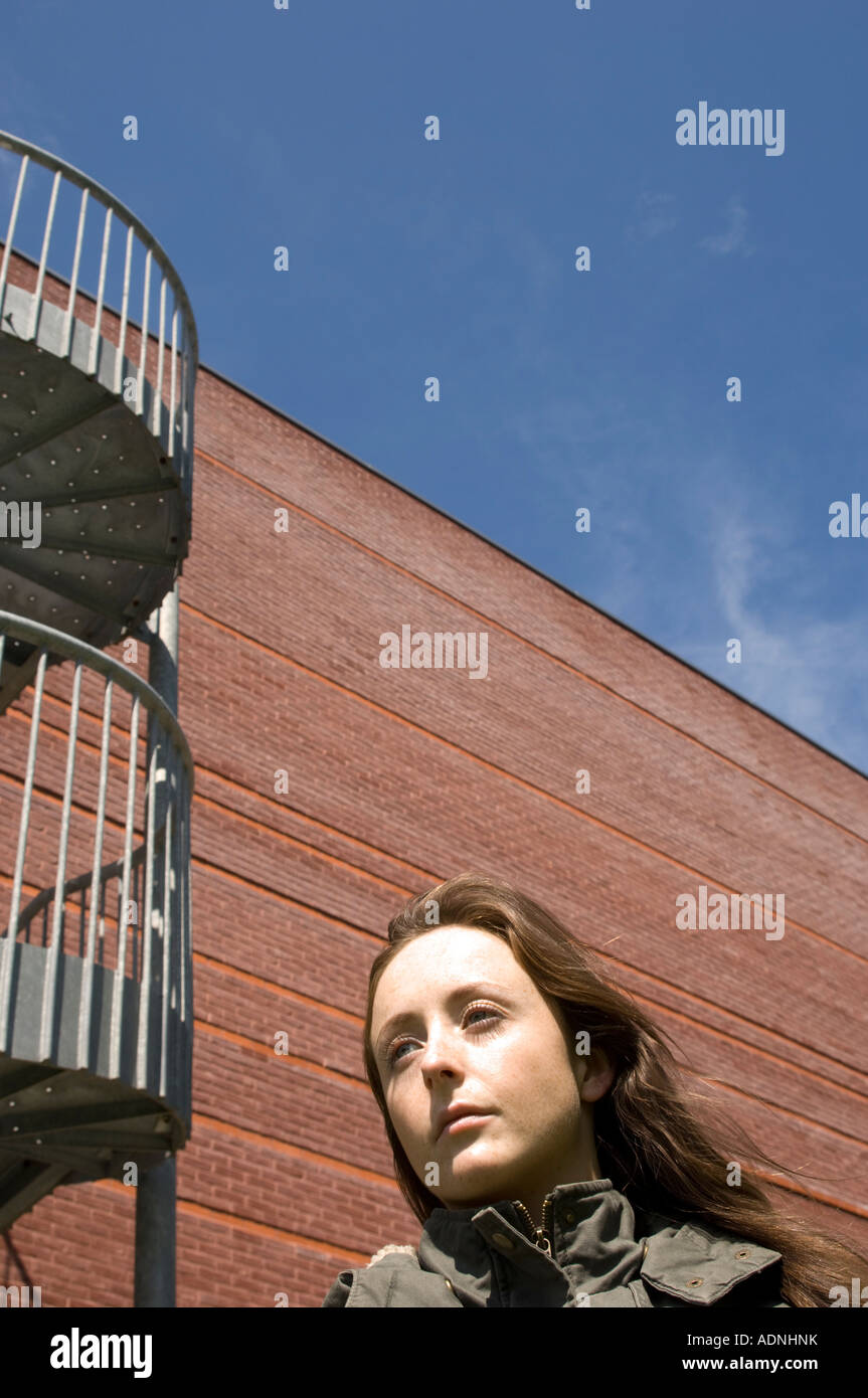 junge Frau mit Spirale Metalltreppe Backsteingebäude hinter ihr; sonnigen Nachmittag klaren blauen Sommerhimmel Stockfoto