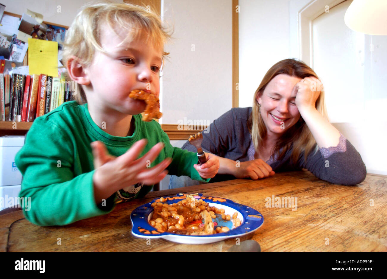 Mama Kleinkind Essen Bohnen-Uhren und verzweifelt an dem Schlamassel Stockfoto