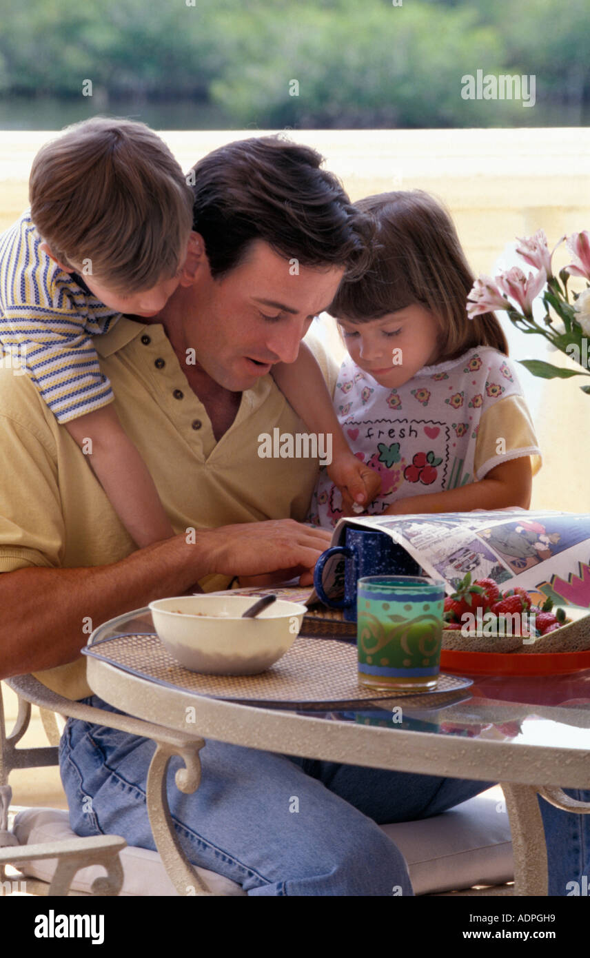 Kaukasische Vater und Kinder Comics lesen, während des Frühstücks Stockfoto