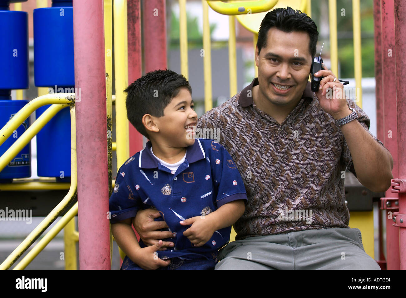 Hispanische Vater auf Handy und Sohn neben ihm Stockfoto