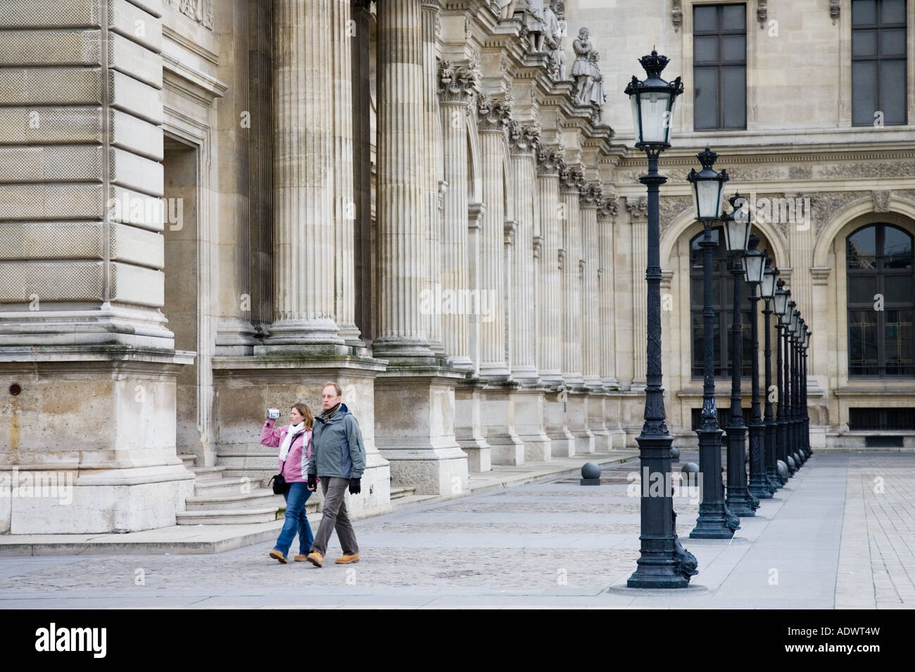 Paar Spaziergang vorbei an einer Reihe von Straßenlaternen durch das Louvre Museum in Paris Frankreich Stockfoto