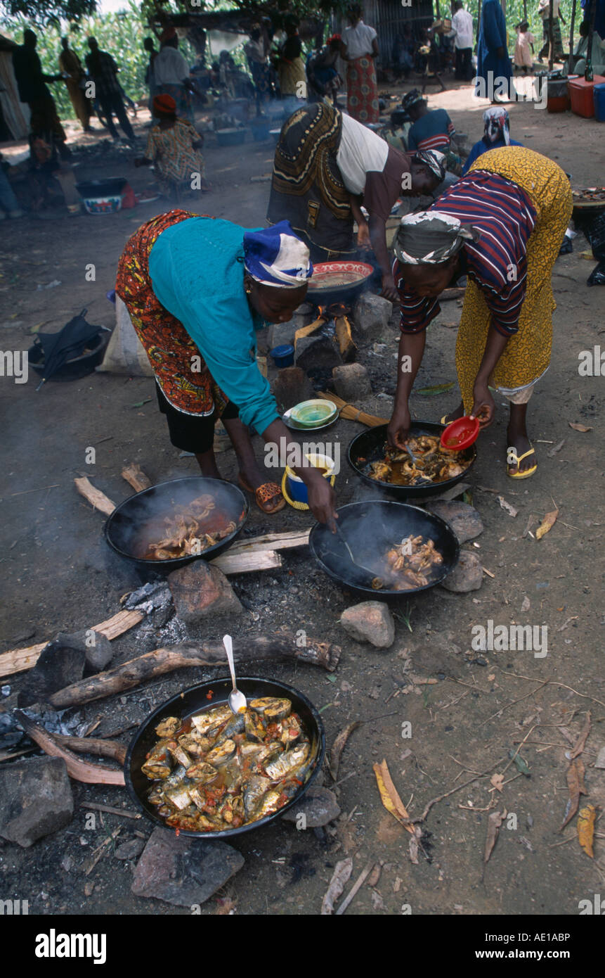 NIGERIA Westafrika Abuja Kochen Essen im Dikko Markt. Frauen unter Rühren, Töpfe und Pfannen der Mahlzeiten kochen auf offenem Feuer am Boden Stockfoto