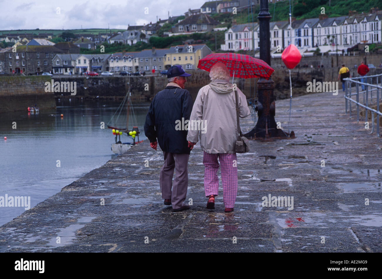 Älteres Ehepaar zu Fuß entfernt von der Kamera bei nassem Wetter mit Regenschirm Porthleven Cornwall England Stockfoto