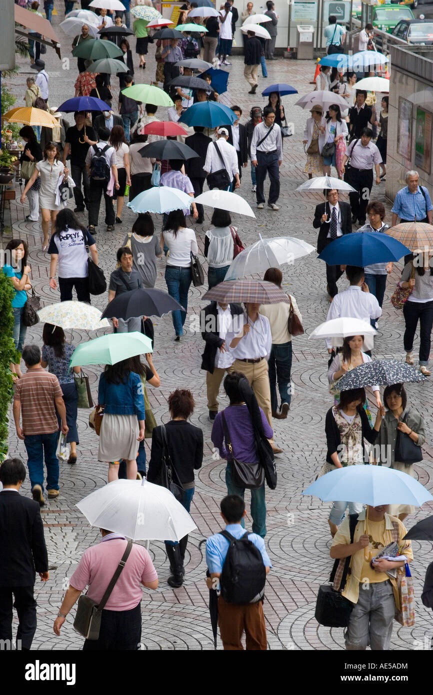 Menschen zu Fuß auf einem überfüllten Bürgersteig halten Sonnenschirme im Regen draußen Shinjuku Bahnhof in Tokio Japan Stockfoto