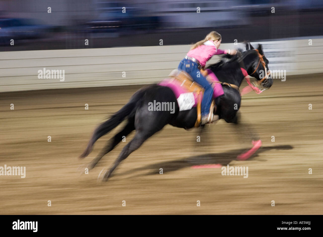 Teenager-Mädchen in Rosa Rennen auf ihrem Pferd in einer Unschärfe, wie sie in einem Fass racing Event konkurrieren gekleidet Stockfoto